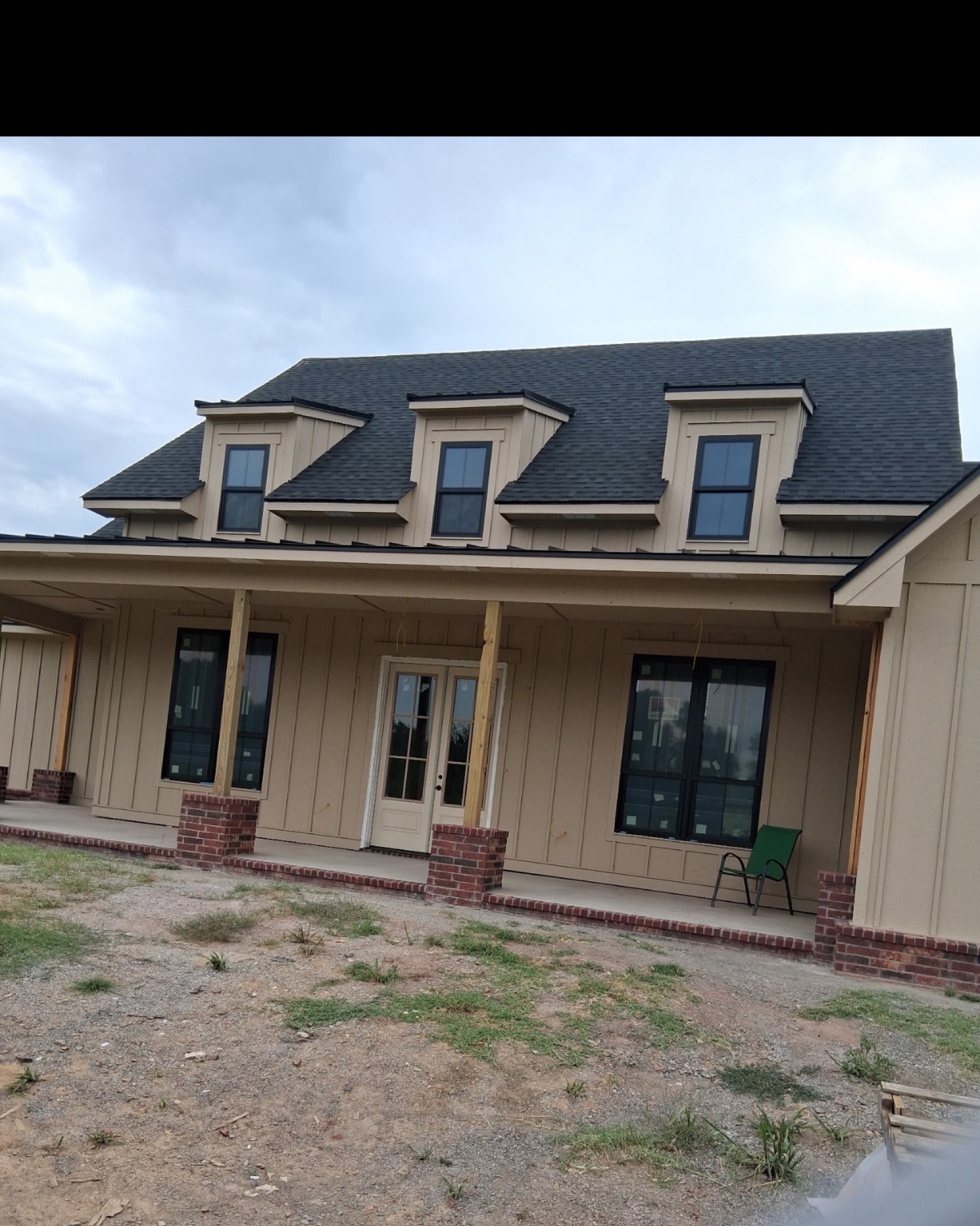 Completed farmhouse with three dormers, board and batten siding, brick porch columns